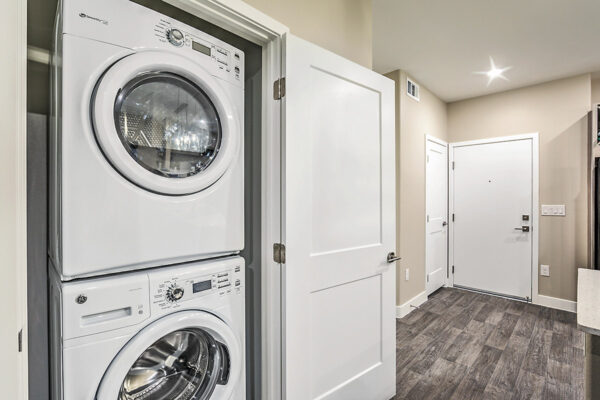 Laundry closet with stacked washer dryer and hallway to entry door.