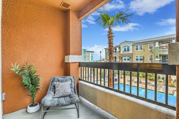 Apartment balcony with chair and potted plant overlooking pool area.