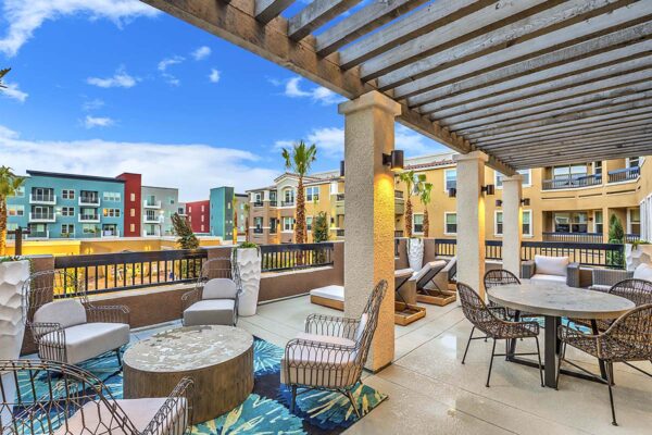 Rooftop lounge with lounge chairs, dining tables, and potted plants overlooking pool area.