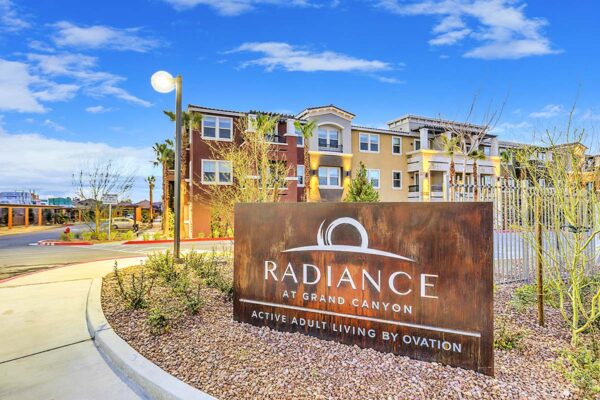 Radiance at Grand Canyon entrance with lush landscaping, tall palms, and rustic monument sign.