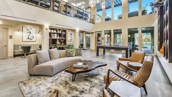 Clubhouse with plush chairs, pool table, shelves with decor, and large windows.