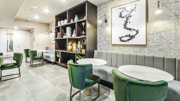 Clubhouse with booths, stone tables, plush chairs, shelves with decor, and large artwork.