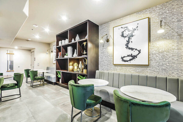 Clubhouse with booths, stone tables, plush chairs, shelves with decor, and large artwork.