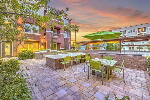 Outdoor grilling area with stone paver patio, built in BBQ grills, and dining tables with umbrellas.