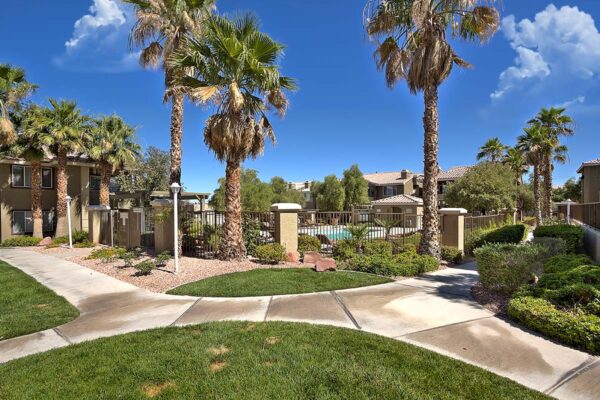 San Croix apartments with paved walkways, lush green lawns, tall palms, and fenced pool area.