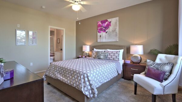 Bedroom with carpet, plush bed, bedside tables with lamps, ceiling fan, and artwork.