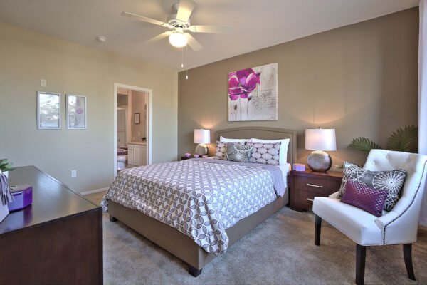 Bedroom with carpet, plush bed, bedside tables with lamps, ceiling fan, and artwork.