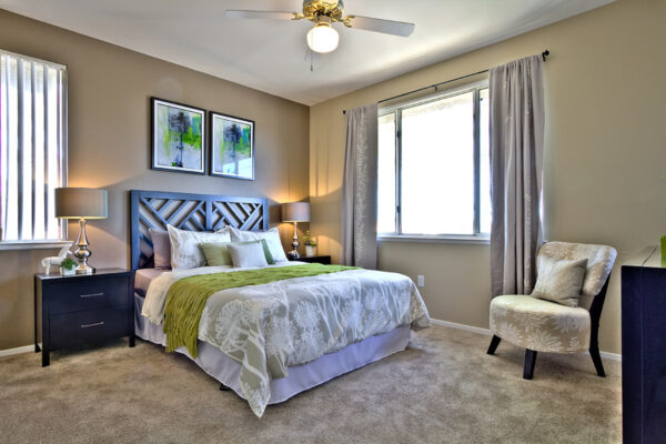 Bedroom with carpet, plush bed, bedside tables with lamps, ceiling fan, and artwork.
