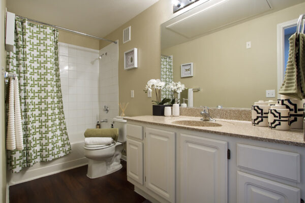 Bathroom with white cabinets, stone counters, large mirror, and tiled shower tub.