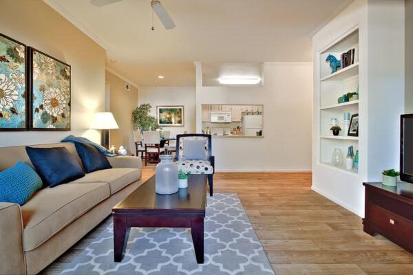 Living room with wood floor, plush couch, coffee table and shelves with decor.