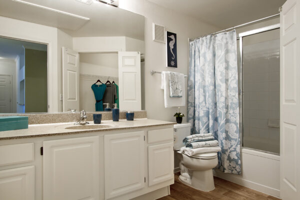 Bathroom with white cabinets, stone counters, large mirror, and tiled shower tub.