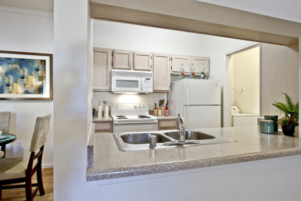 Kitchen with light cabinets, stone counters, white appliances, and laundry closet.