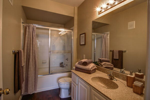 Bathroom with white cabinets, stone counters, large mirror, and tiled shower tub.