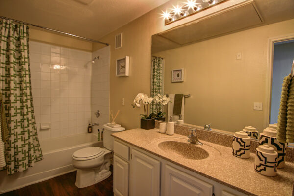 Bathroom with white cabinets, stone counters, large mirror, and tiled shower tub.