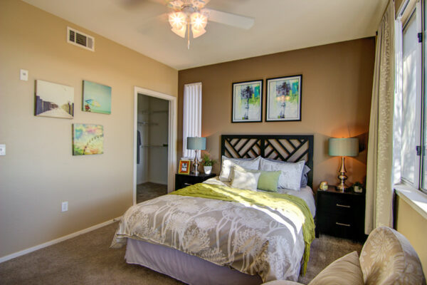 Bedroom with carpet, plush bed with headboard, bedside tables with lamps, and artwork.
