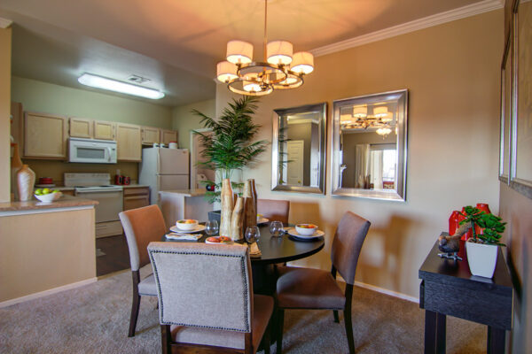Dining room with carpet, round dining table with chairs, framed mirrors, and light fixture.