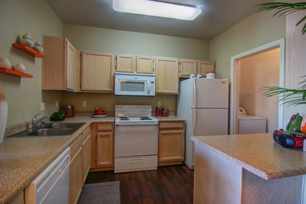 Kitchen with wood floor and cabinets, stone counters, white appliances, and laundry closet.