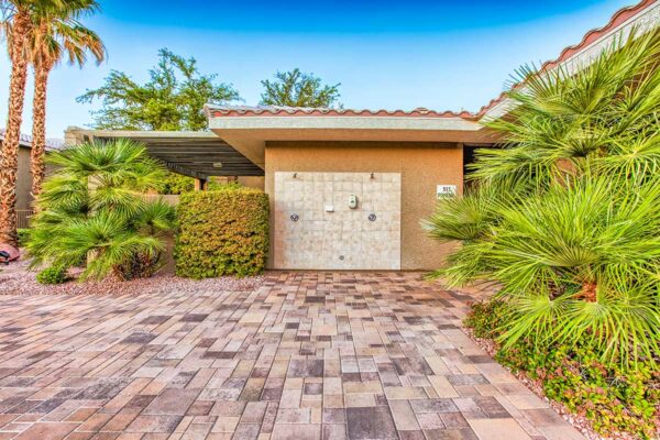 Pool area with stone paver patio, lush landscaping with palm trees, and outdoor shower.
