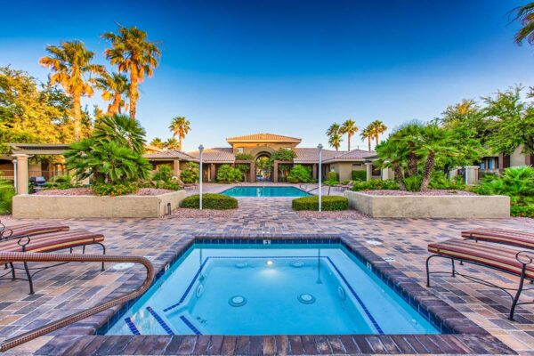 Pool area with spa, lounge chairs, lush landscaping, and tall palms.