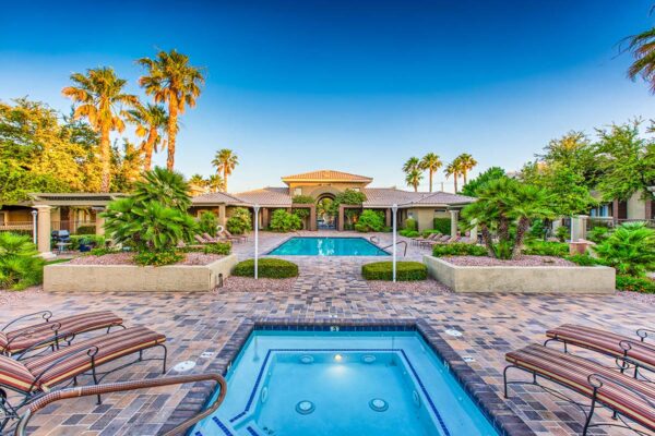 Pool area with spa, lounge chairs, lush landscaping, and tall palms.