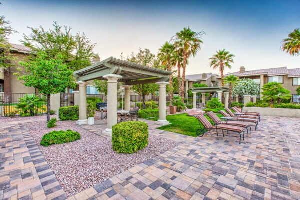 Outdoor lounge with stone paver patio, lounge chairs, and gazebo with table and BBQ grill.