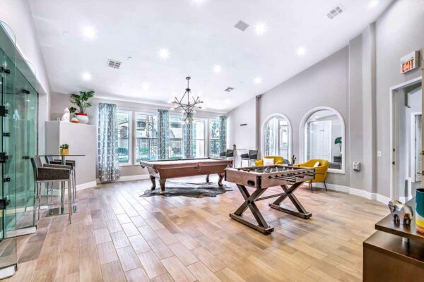 Lounge with pool table, foosball table, plush chairs, table with stools, and large windows.
