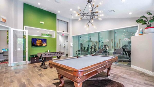 Lounge with pool table, foosball table, TV, table with stools, and large windows.