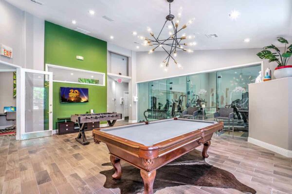 Lounge with pool table, foosball table, TV, table with stools, and large windows.