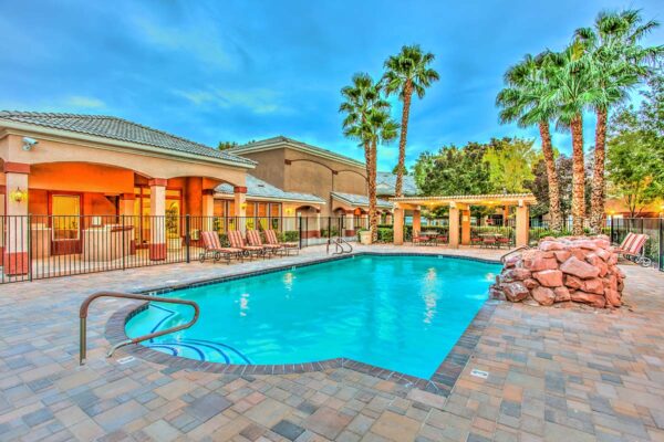 Swimming pool with rock waterfall, lounge chairs, metal fence, and tall palm trees.