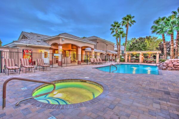 Swimming pool with rock waterfall, lounge chairs, metal fence, and tall palm trees.