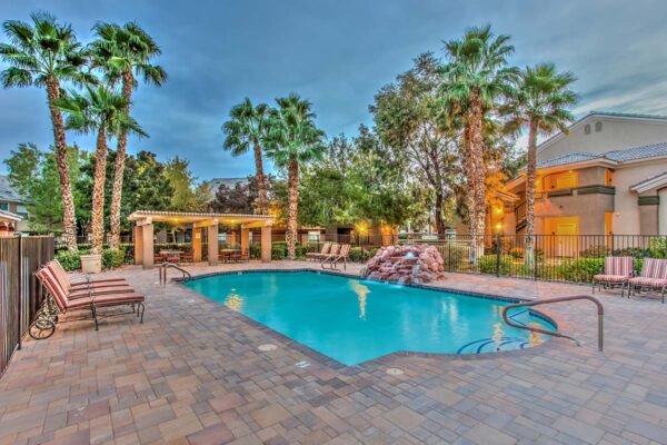 Swimming pool with rock waterfall, lounge chairs, metal fence, and tall palm trees.