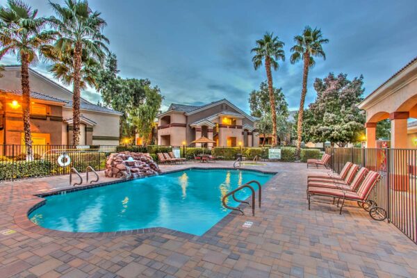 Swimming pool with rock waterfall, lounge chairs, metal fence, and tall palm trees.