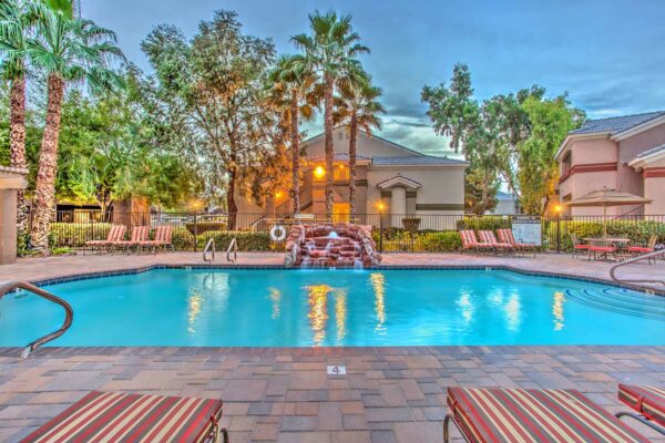 Swimming pool with rock waterfall, lounge chairs, metal fence, and tall palm trees.