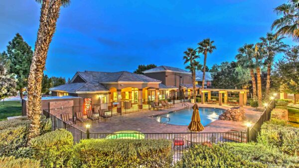 Fenced pool area with lounge chairs, pergola, rocky waterfall, and tall palm trees.