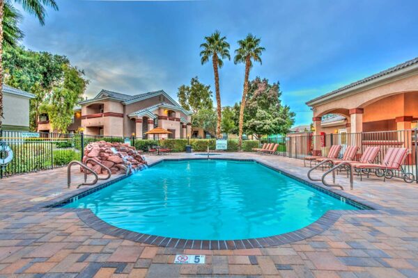 Swimming pool with rock waterfall, lounge chairs, metal fence, and tall palm trees.