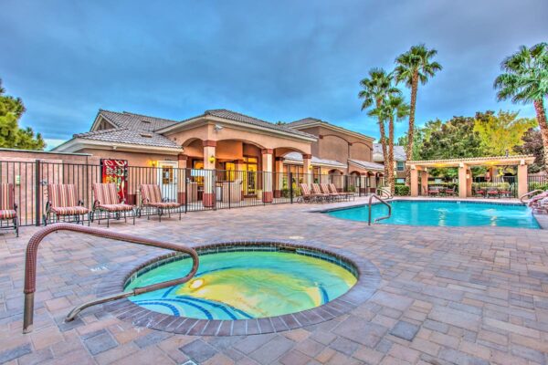 Swimming pool with rock waterfall, lounge chairs, metal fence, and tall palm trees.