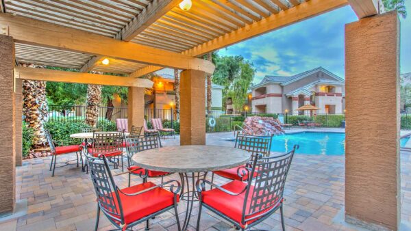 Pool area with pergola, dining tables with chairs, lounge chairs, and pool with waterfall.