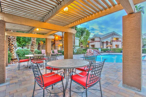 Pool area with pergola, dining tables with chairs, lounge chairs, and pool with waterfall.