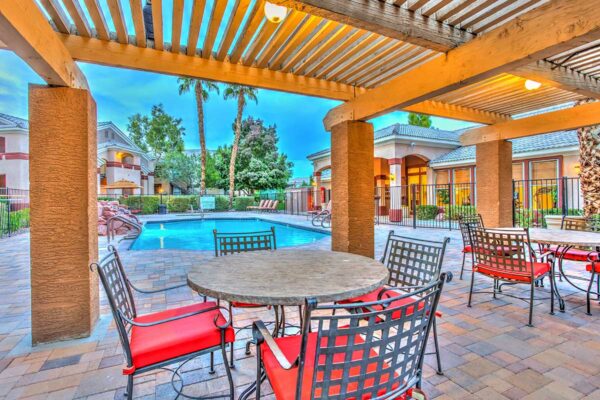 Pool area with pergola, dining tables with chairs, lounge chairs, and pool with waterfall.