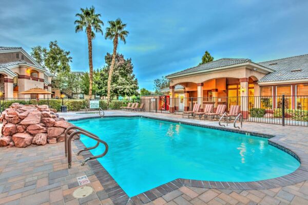 Swimming pool with rock waterfall, lounge chairs, metal fence, and tall palm trees.