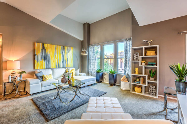 Living room with carpet, plush sectional, bookshelf with decor, floor standing lamp, and vaulted ceilings.