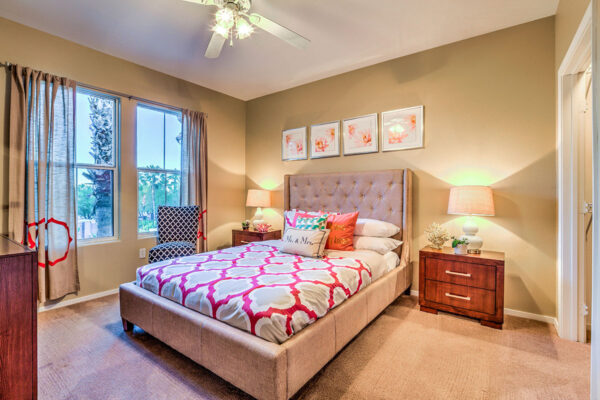 Bedroom with carpet, plush bed with headboard, bedside drawers with lamps, and large windows.