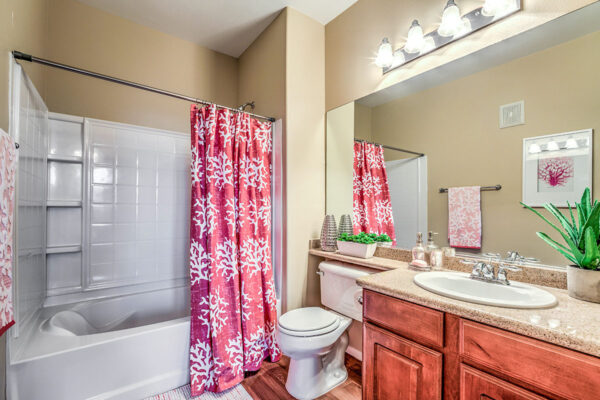 Bathroom with wood style floor, wood cabinets, large mirror, and tiled shower tub.