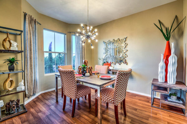 Dining room with wood style floor, dining table with pattern chairs, lighting fixture, and large windows.
