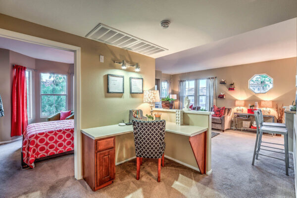 Living area with plush carpet, breakfast bar, built in corner desk, and door to bedroom.