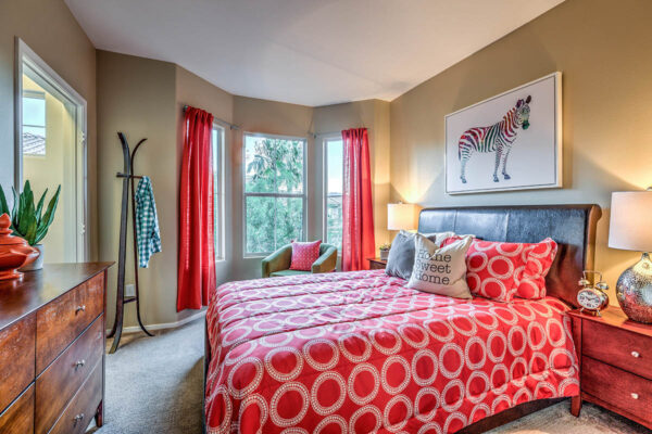 Bedroom with carpet, plush bed with headboard, bedside drawers with lamps, and large windows.