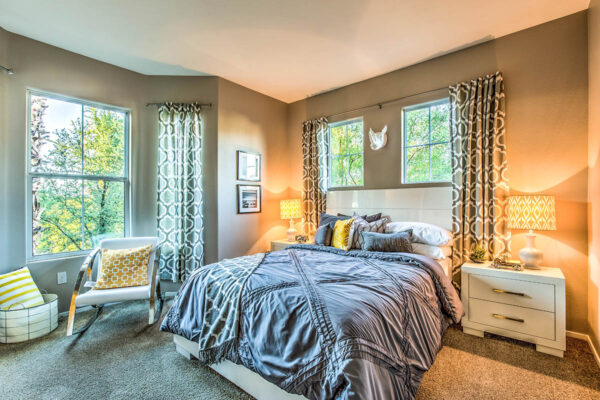 Bedroom with carpet, plush bed with headboard, bedside drawers with lamps, and large windows.
