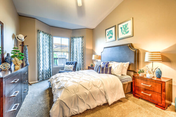 Bedroom with carpet, plush bed with headboard, bedside drawers with lamps, and large windows.