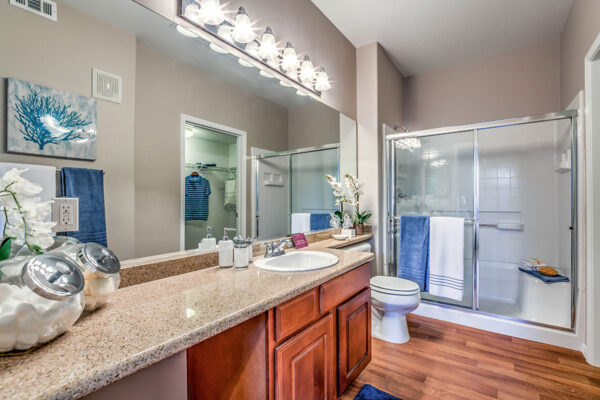 Bathroom with wood style floor, wood cabinets, large mirror, and tiled shower.