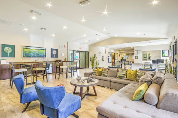 Clubroom with plush seating, coffee table with decor, and dining tables with tall chairs.